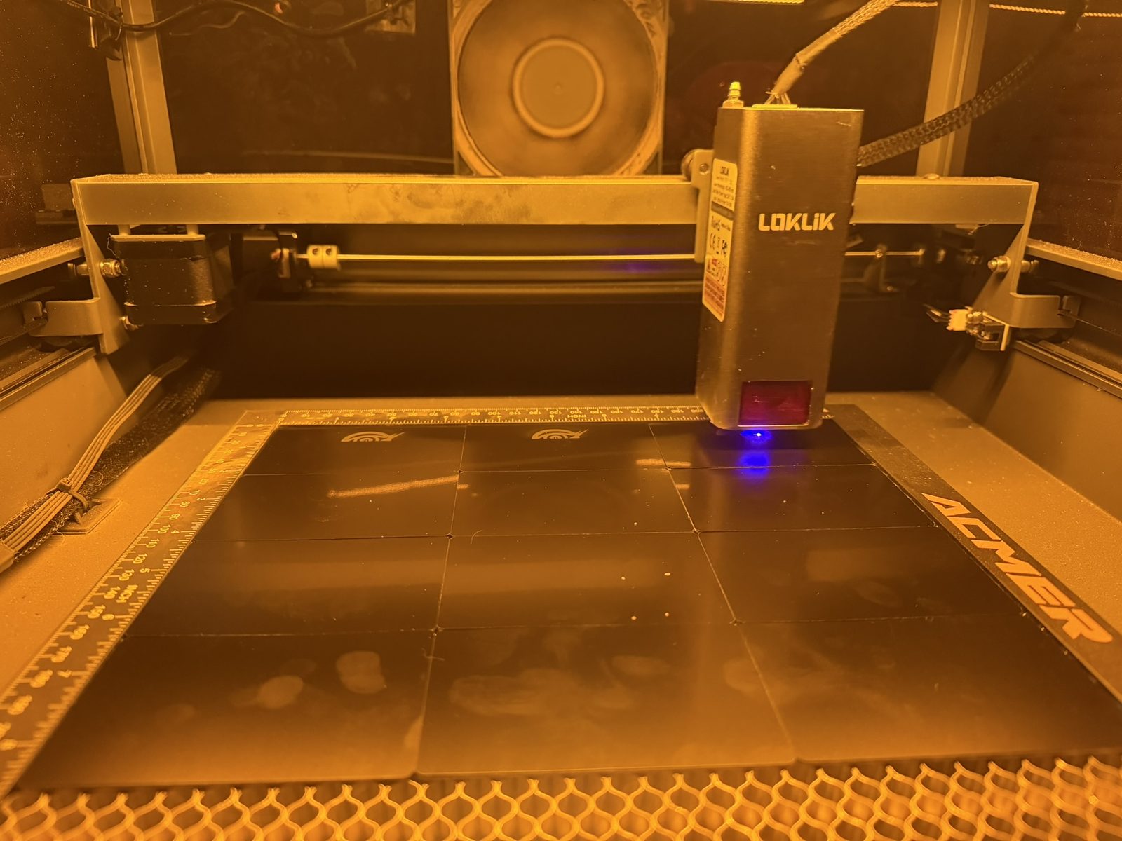 LOKLIK laser firing a blue beam onto black tiles inside the ACMER enclosure